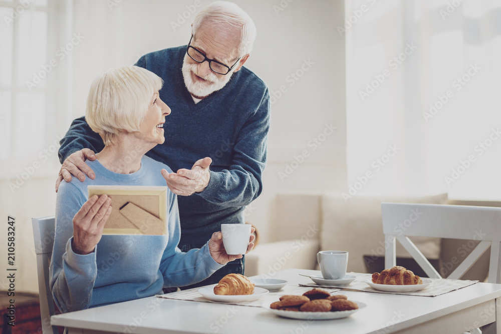 Family relationships. Happy senior man talking to his wife while discussing a photo Family relationships. Happy senior man talking to his wife while discussing a photo