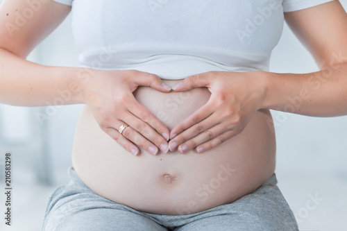 Wallpaper Mural Close-up of pregnant woman holding hands in a heart shape on her belly. Maternity concept. Healthy pregnancy and lifestyle Torontodigital.ca