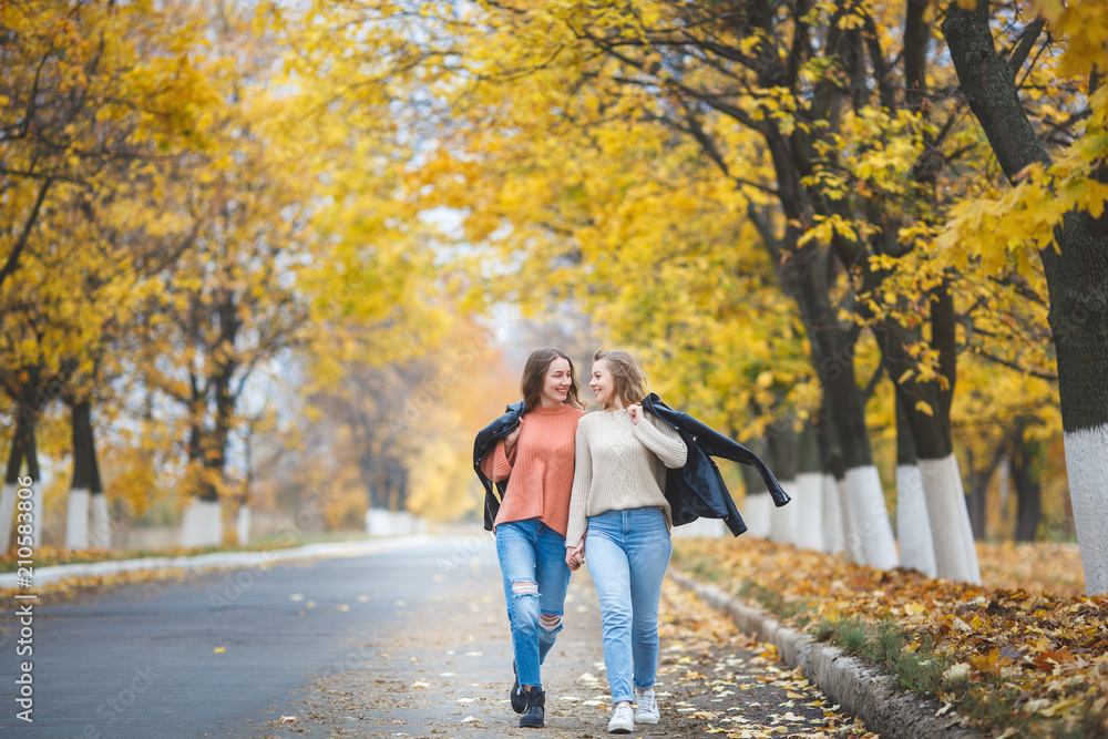 Young pretty girls having fun outdoors in autumn background. Cheerful friends in the fall time Young pretty girls having fun outdoors in autumn background. Cheerful friends in the fall time