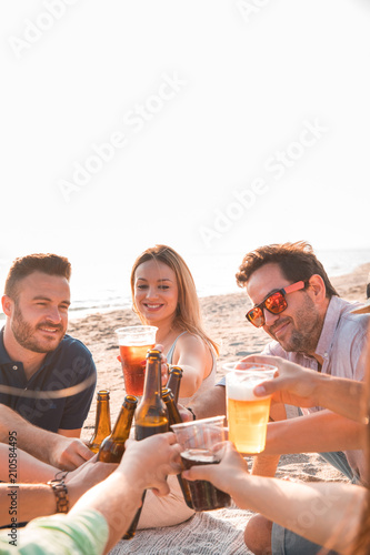 Cheers! Group of happy young people are toasting with bottles of beer in the beach. Celebration and holiday concept