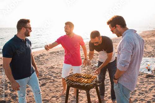 Happy friends are having fun while they are preparing a barbecue on the beach. Vacation concept. photo