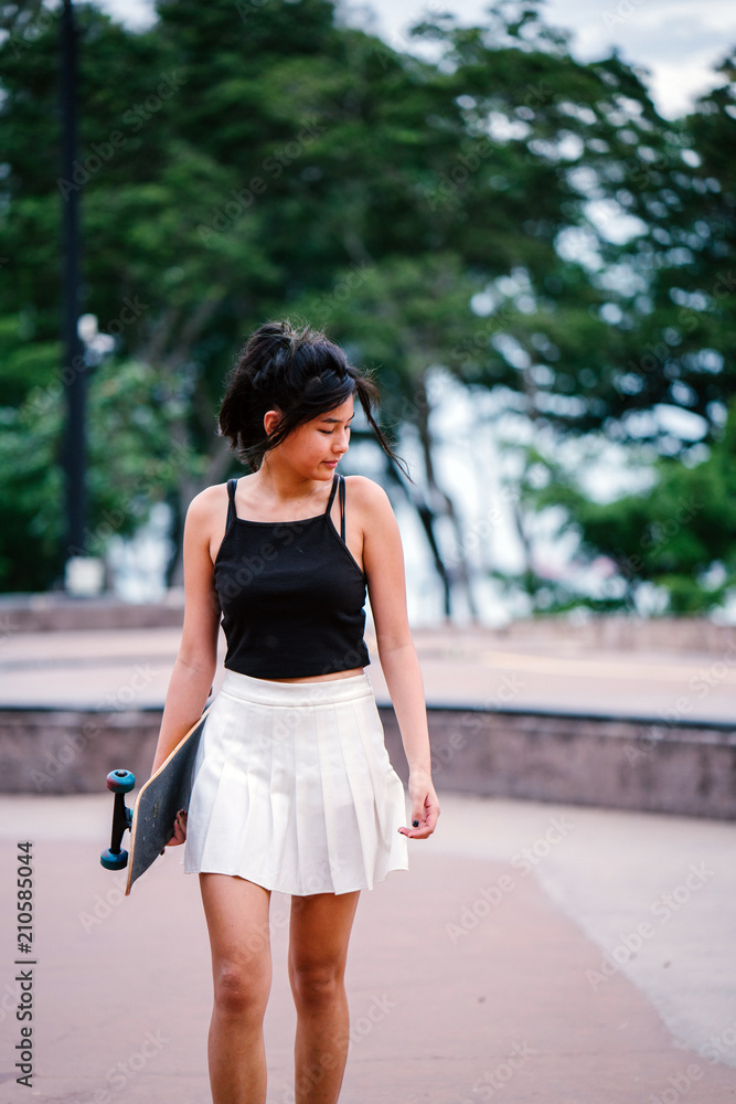 Portrait of an Asian Chinese girl with her skateboard at a skate park. She is pretty, sporty, attractive and too-cool-for-school. 