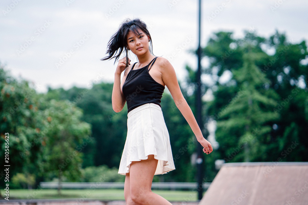 A portrait of a young Chinese Asian teenager twirling and whirling happily in the skate park during the day. 
