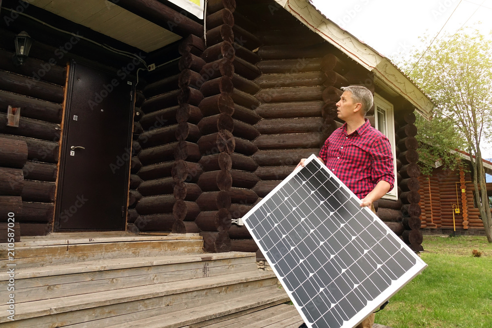 Solar panels in the hands of men . Energy production technologies. Wooden house background. Solar panels in the hands of men . Energy production technologies. Wooden house background.