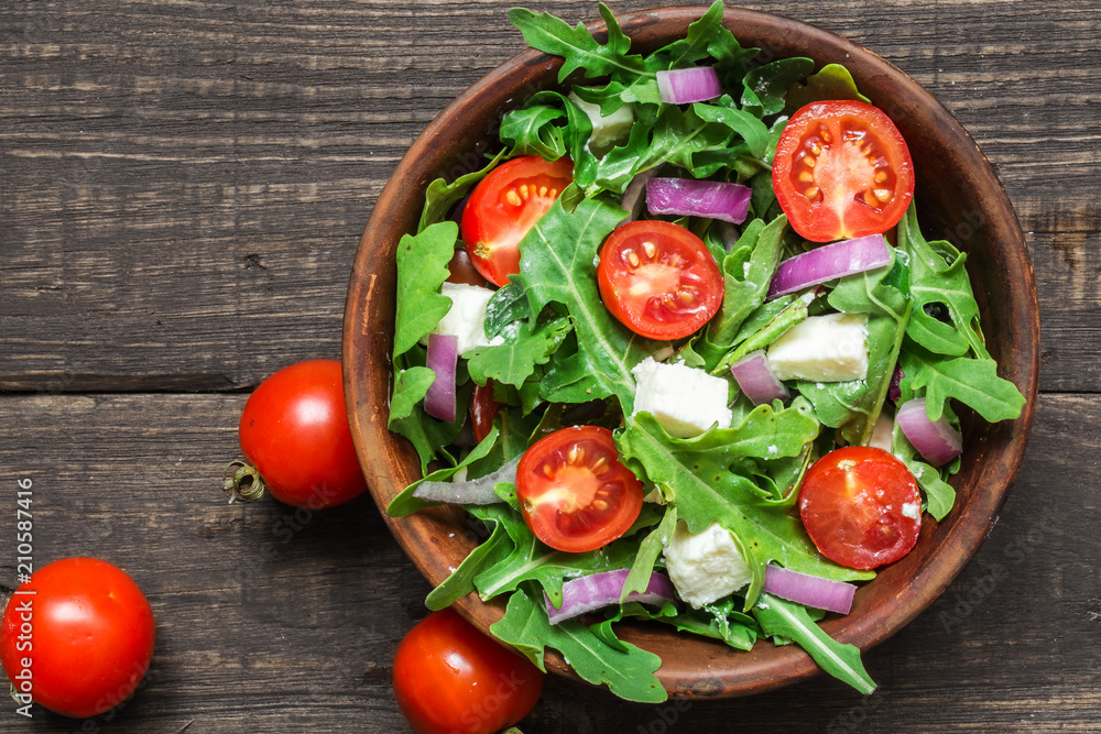 Fresh salad with rucola, tomatoes cherry, feta cheese and red onion in a bowl on rustic wooden table. top view Fresh salad with rucola, tomatoes cherry, feta cheese and red onion in a bowl on rustic wooden table. top view