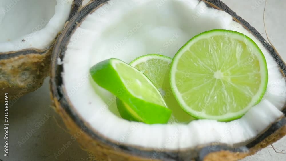 Limes slices fall into a coconut half in slow motion. The fresh citrus
