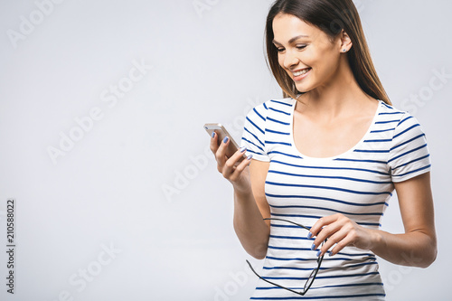 Portrait of cheerful beautiful young woman using mobile phone. Smiling, isolated over white wall background.