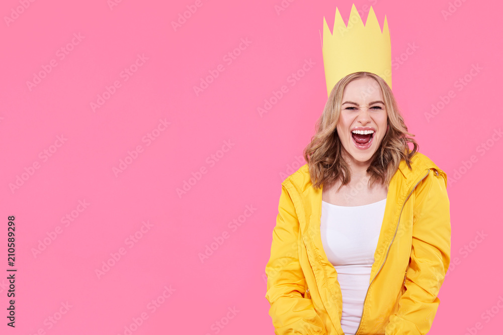 Beautiful teenage girl in bright yellow jacket and party hat shouting with excitement. Attractive cool young woman fashion portrait over pastel pink background. Beautiful teenage girl in bright yellow jacket and party hat shouting with excitement. Attractive cool young woman fashion portrait over pastel pink background.