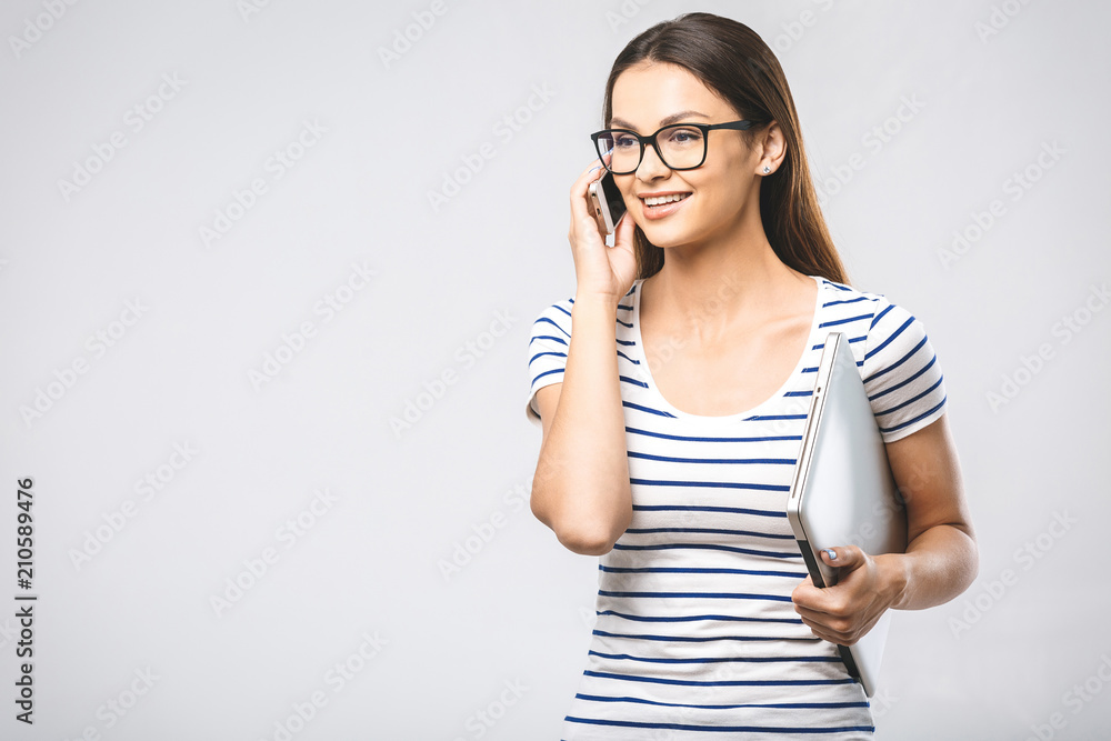 Portrait of cheerful beautiful young woman with laptop using mobile phone. Smiling, isolated over white wall background. Portrait of cheerful beautiful young woman with laptop using mobile phone. Smiling, isolated over white wall background.