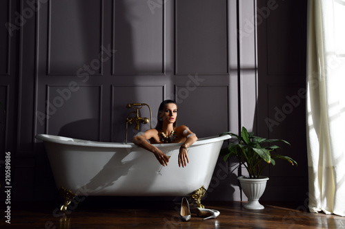 Young beautiful woman sitting in bathroom near expensive bathtub bath looking at the corner on dark 