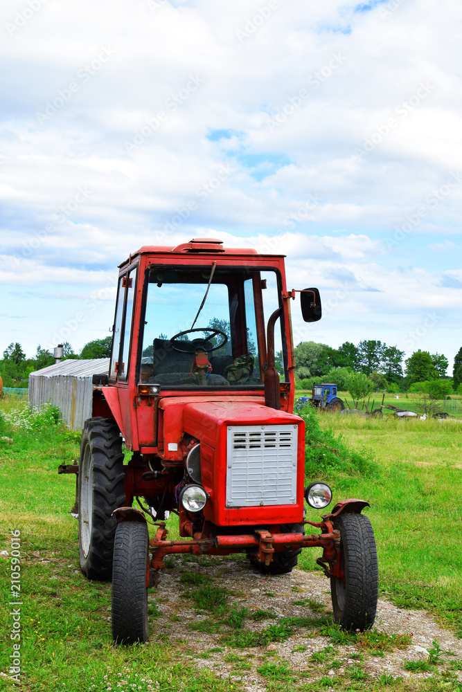 Old red tractor on green grass and blue sky background on yard in sunny summer day. Old red tractor on green grass and blue sky background on yard in sunny summer day.
