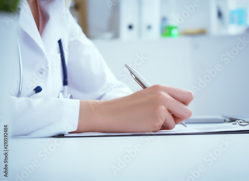 Front view of female doctor holding silver pen filling patient history list at clipboard pad. Physical exam or disease prevention.