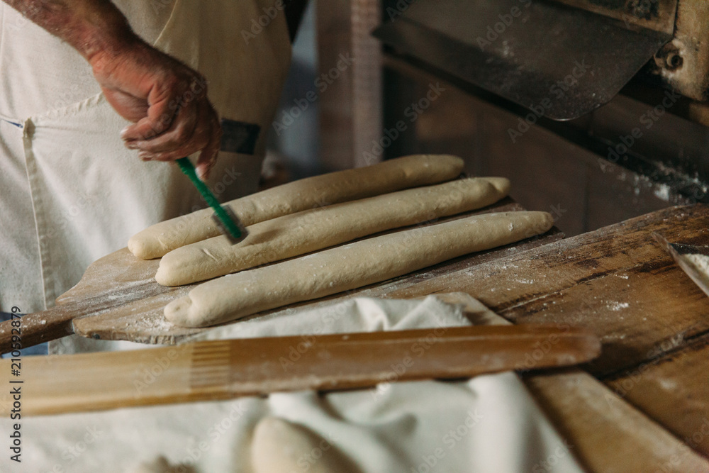 Baker is preparing the raw dough bread before baking in a wood oven. Traditional Bakery Concept.