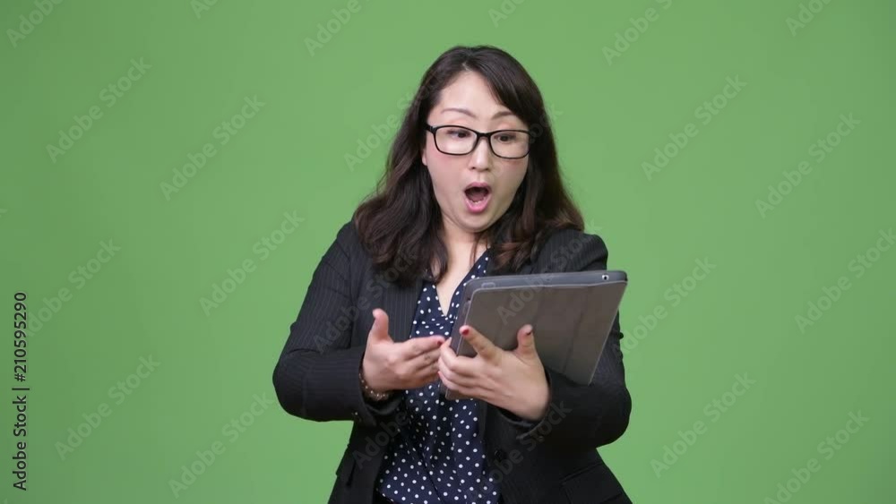 Mature beautiful Asian businesswoman looking shocked while using digital tablet Mature beautiful Asian businesswoman looking shocked while using digital tablet
