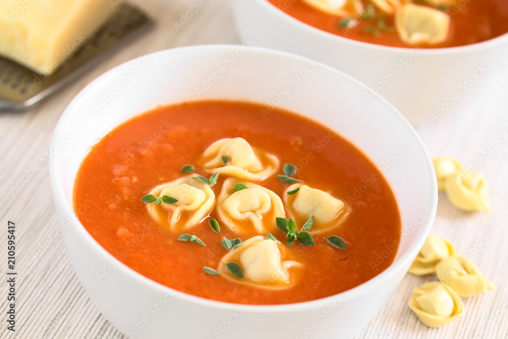 Homemade fresh cream of tomato soup with tortellini garnished with fresh oregano leaves, photographed with natural light (Selective Focus, Focus in the middle of the first soup) Homemade fresh cream of tomato soup with tortellini garnished with fresh oregano leaves, photographed with natural light (Selective Focus, Focus in the middle of the first soup)