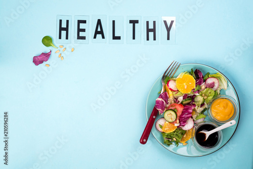 Fresh salad with fruits and greens on blue background