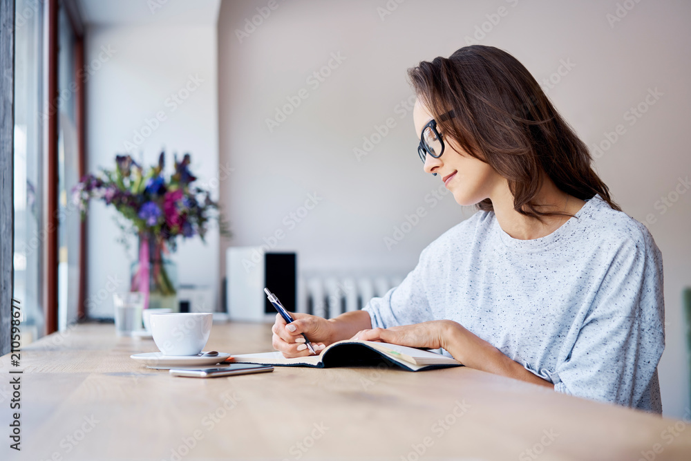 Young student writing in notebook while having coffee in a cafe Young student writing in notebook while having coffee in a cafe