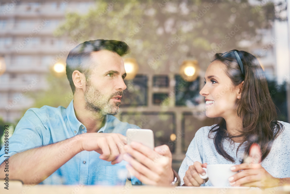 Couple talking and using smartphone while having coffee in cafe Couple talking and using smartphone while having coffee in cafe