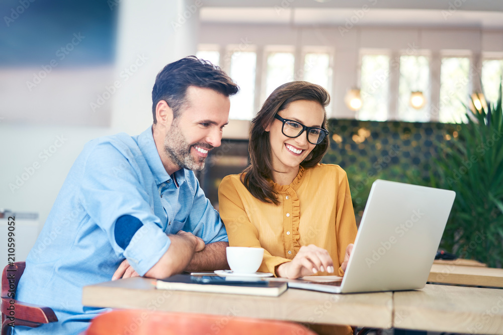 Joyful couple using laptop while having coffee in cafe together Joyful couple using laptop while having coffee in cafe together