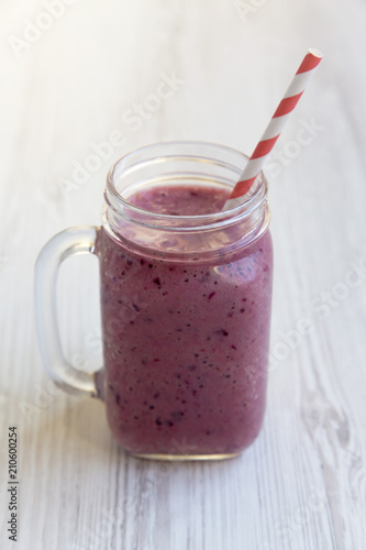 Mason jar mug with smoothie on a white wooden table, side view.