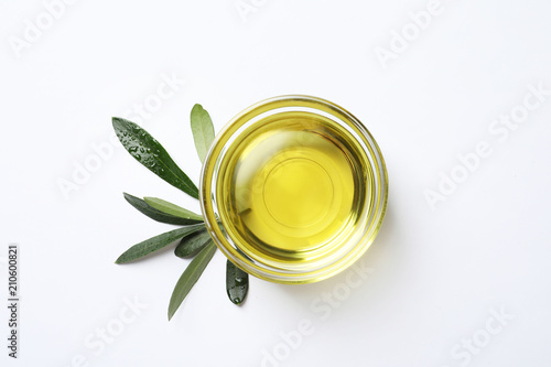Little bowl with fresh olive oil and leaves on white background