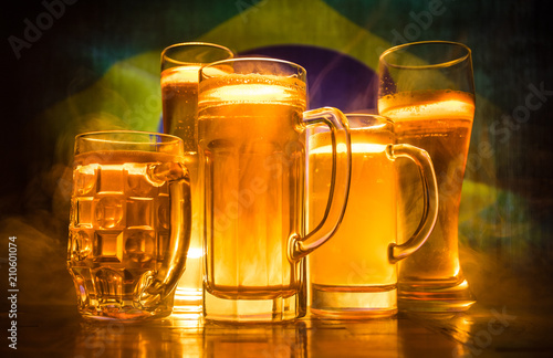 Creative concept. Beer glasses on table at dark toned foggy background with blurred view of flag of Brazil. Support your country with beer concept.