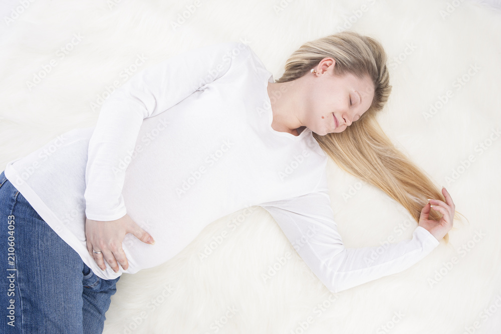 Positive and Tranquil Relaxing Pregnant Woman Laying on Fur Carpet In White Shirt and Jeans. Dreaming with Eyes Closed Positive and Tranquil Relaxing Pregnant Woman Laying on Fur Carpet In White Shirt and Jeans. Dreaming with Eyes Closed