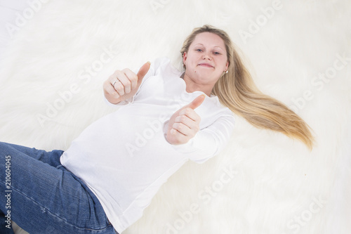 Family and Child-Bearing Concepts. Tranquil Relaxing Pregnant Woman Laying on Fur Carpet In White Shirt and Jeans.Showing Thumbs Up photo