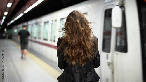 Attractive woman in an underground subway station checking her phone as a train arrives in slow motion