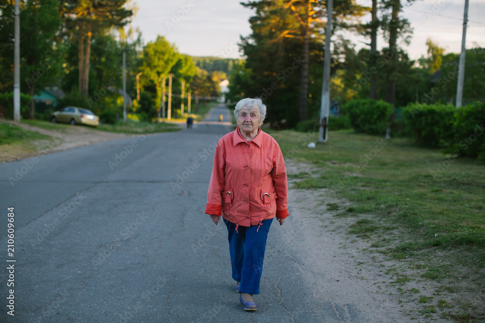 An elderly woman is walking down the street in the village. An elderly woman is walking down the street in the village.