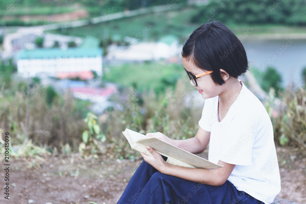 Obraz premium Little kid whit glasses reading a book on mountain