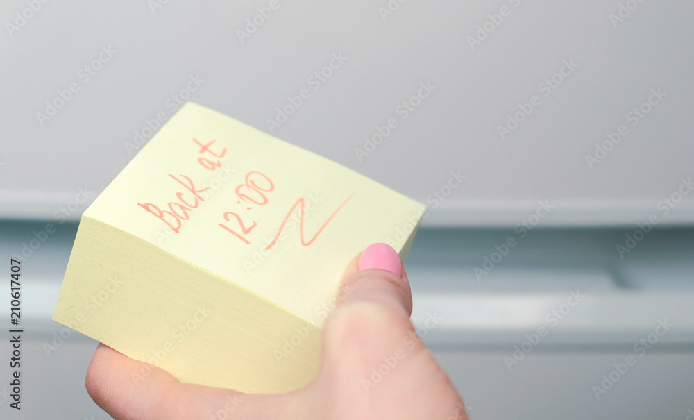 Yellow sticker paper sheet with words back at 12 in woman's hand. Yellow sticker paper sheet with words back at 12 in woman's hand.