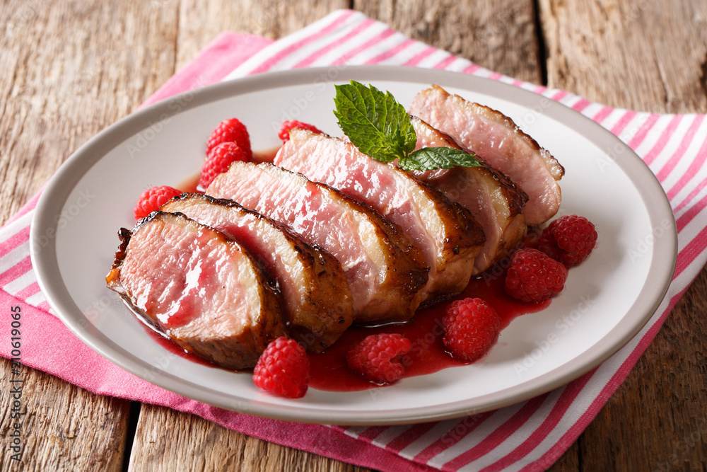festive food: sliced grilled duck breast with raspberry sauce and mint closeup on a plate on the table. horizontal
