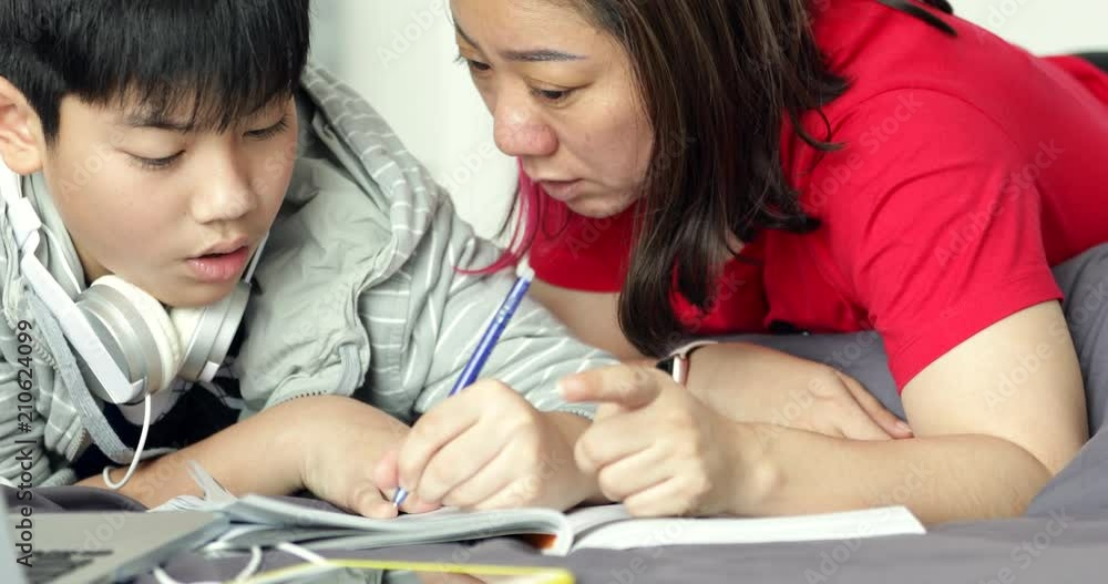 Asian mother helps his young son while the boy is doing his homework at home. Asian mother helps his young son while the boy is doing his homework at home.