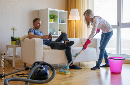 Woman cleaning home and man doesn't help her photo