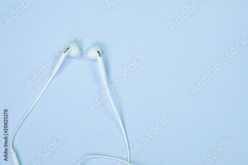 White Earphones or ear buds small talk on sweet blue colour pastel paper, top view, texture and background. music listening concept.