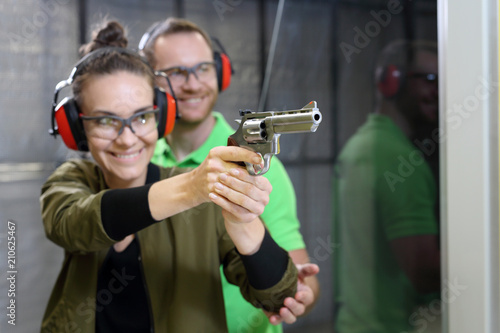 Strzelanie rekreacyjne na strzelnicy. Kobieta strzela z rewolweru pod okiem instruktora.