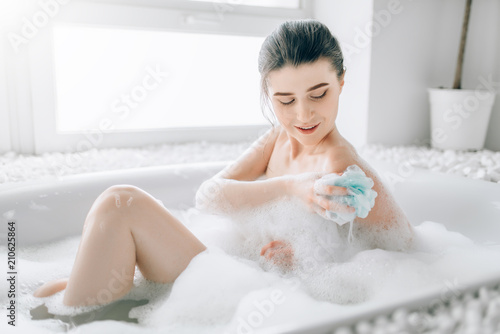 Young woman soaps the body with a sponge