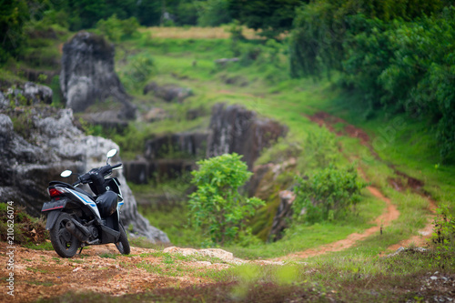 A parked scooter stands on a background of nature with a trail going away and rocks