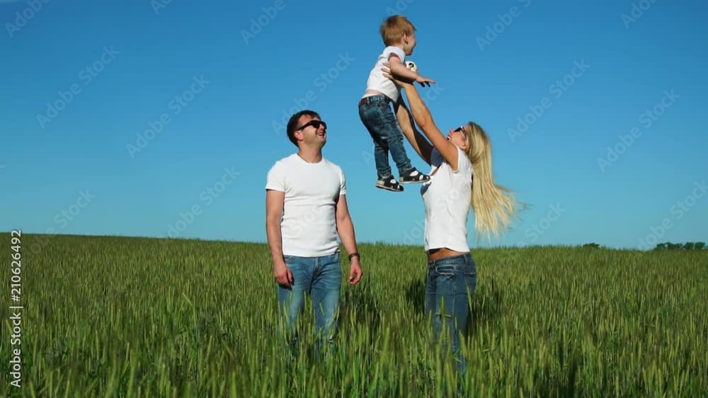 Happy family: Father mother and son jump and laugh in the field wearing white t-shirts and jeans Happy family: Father mother and son jump and laugh in the field wearing white t-shirts and jeans