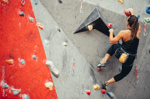 Sporty strong young woman in black outfit exercising in boulder climbing hall reaching new results, enjoying new challenges.