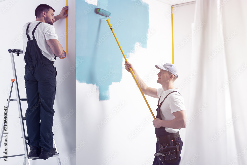 Man with roller painting white wall on blue while finishing interior Man with roller painting white wall on blue while finishing interior