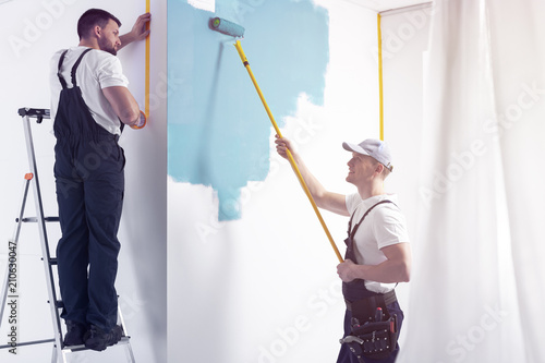 Man with roller painting white wall on blue while finishing interior