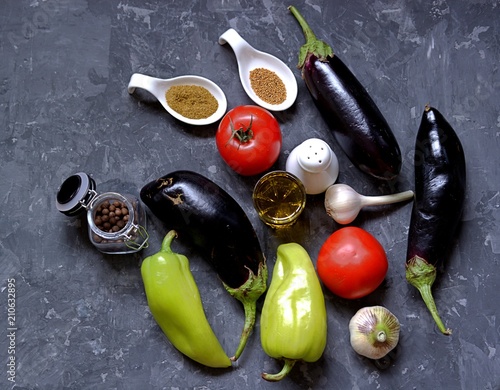 ngredients for preparation of salad  from eggplants, tomatoes and sweet peppers on a dark gray concrete background. Eggplants, tomatoes, sweet peppers, garlic, spices, salt, olive oil. photo