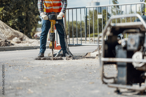 Canvas Print Craftsman in uniform with drill repairing asphalt during roadwork