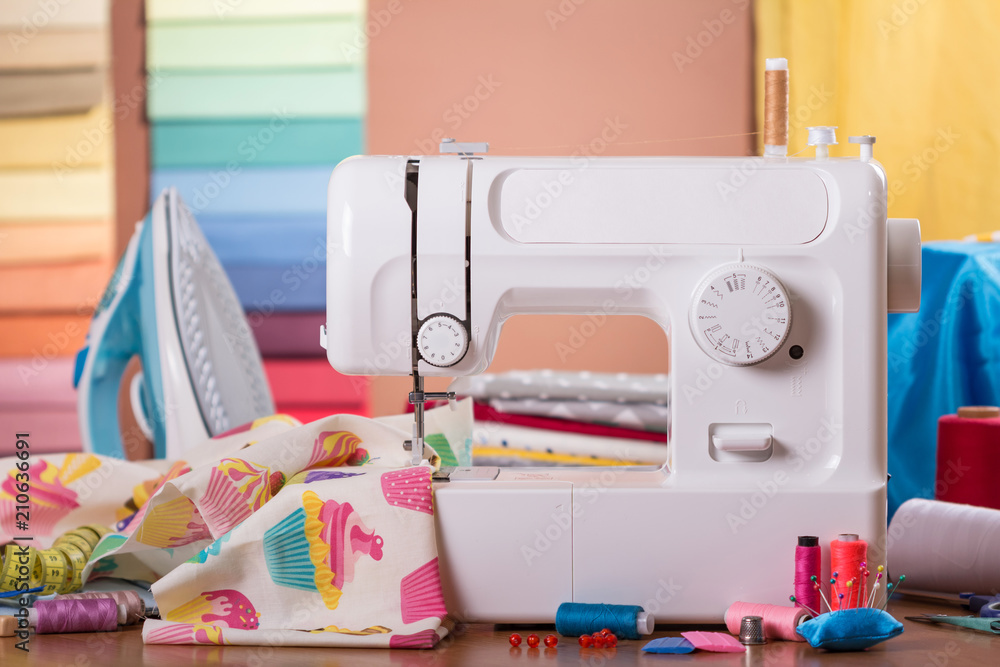 Sewing machine in work and accessories, on background of fabric samples