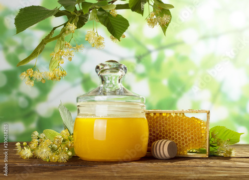 Jar of honey and honeycomb on wooden table under Linden branch