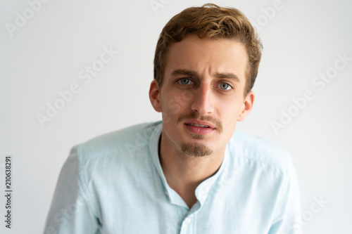 Focused guy in white casual shirt discovering hidden camera. Closeup of young Caucasian blonde man staring at camera attentively. Candid camera concept