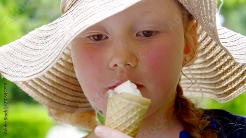 small caucasian girlie is eating ice cream in a waffle cone in a park in summer day, close-up of her face