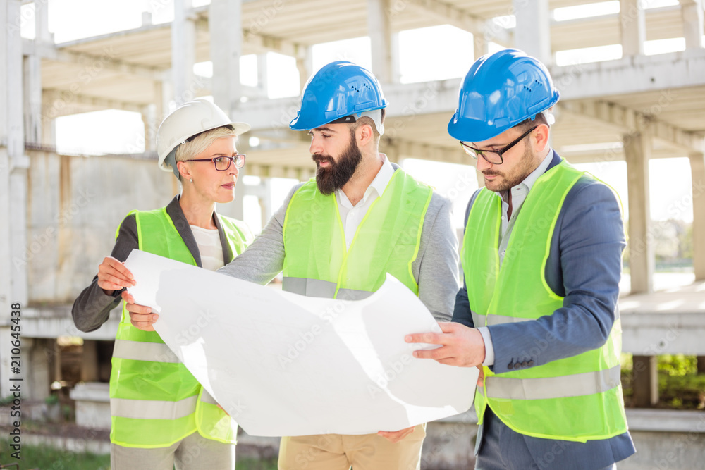 Mixed group of architects or business partners at construction site, working together on building's blueprint. Architecture and teamwork concept. Mixed group of architects or business partners at construction site, working together on building's blueprint. Architecture and teamwork concept.
